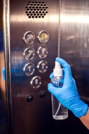 Woman with medicine gloves doing desinfection of buttons in the elevator with antiseptic spray. Close up. Hygiene and virus protection conceptの写真素材