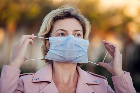 A portrait of woman with short blond hair with medical face mask outdoor. People, healthcare and...