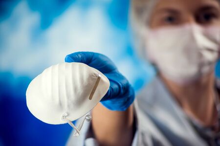 A female doctor holds medical mask in hand and shows it at camera. Medicine and healthcare concept.の写真素材
