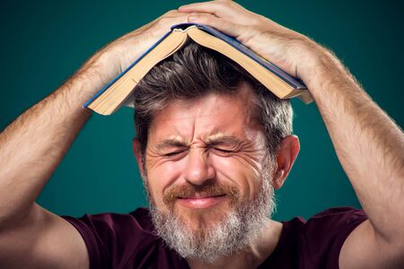 A portrait of bearded man in red t-shirt holding opened book on head. People, education and searching conceptの写真素材