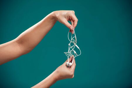 Woman holding white tangled earphone trying to untangle it. People and technology conceptの写真素材