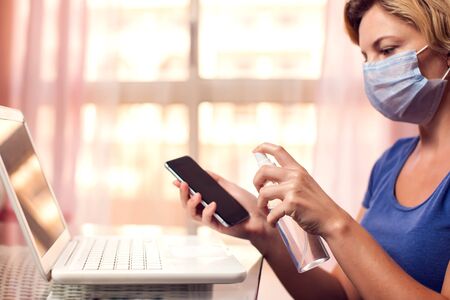 Woman cleaning smartphone with antiseptic spray. Hygiene conceptの写真素材