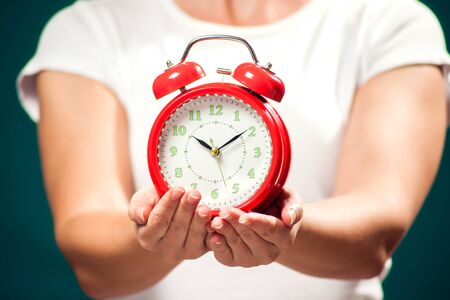 Woman holding red alarm clock. Close-up shot
