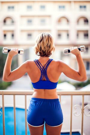 Woman with short blond hair doing exercices with dumbbells on the balcony. People, fitness and lifestyle concept.の写真素材