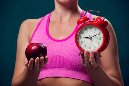 Woman in sportswear holding alarm clock and apple. People, fitness and dieting conceptの写真素材