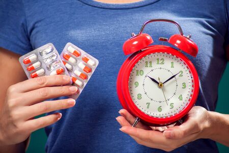 A portrait of woman holding red alarm clock and pills. Healthcare and medicine conceptの写真素材