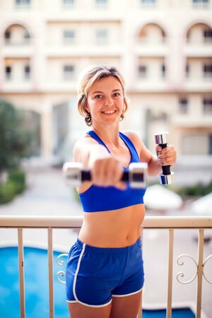 Woman with short blond hair doing exercices with dumbbells on the balcony. People, fitness and lifestyle concept.の写真素材