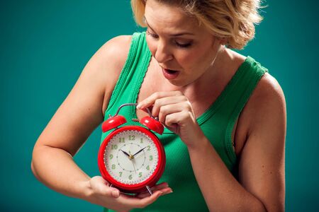 A portrait of surprised woman holding red alarm clock. People and emotions concept