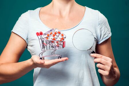 Woman holding small shopping trolley with pills and magnifier. Healthcare and medicine conceptの写真素材