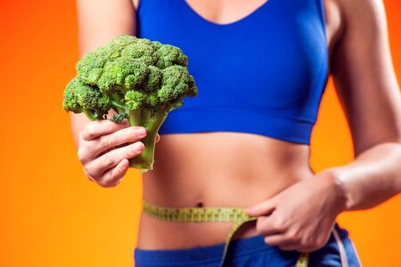 Woman measuring waist and holding broccoli. People, fitness and dieting conceptの写真素材