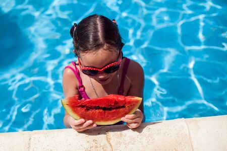 Kid girl eating watemelon beside swimming pool. Childhood, summer and holiday conceptの写真素材