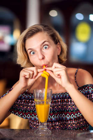 A portrait of smiling young woman with short blond hair with funny face drinking mango juice in the cafe. People, emotions and lifestyle conceptの写真素材
