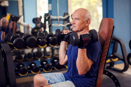 A portrait of bald senior man in the gym training with dumbbells. People, health and lifestyle conceptの写真素材