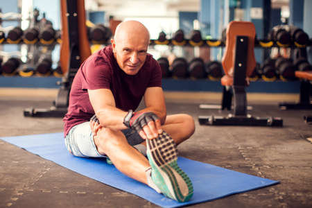 A portrait of bald senior man doing stretching after training in the gym. People, healthcare and lifestyle conceptの写真素材