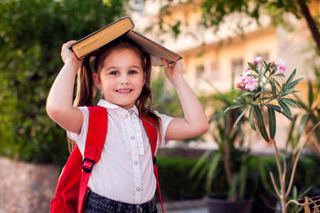 Back to school. Pupil girl with book and backpack staying outdoorの写真素材