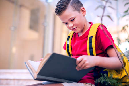 Back to school. Pupil reading book outdoor. Childhood and knowledge concept