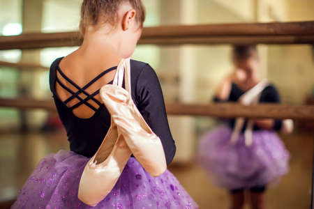Kid girl at dance class holding pointe shoes and staining tears after hard training. Children and sport conceptの写真素材
