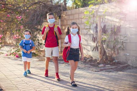 Pupils with medical masks on face and backpacks outdoor. Education during coronavirus time. Children and healthcare. Back to school.の写真素材