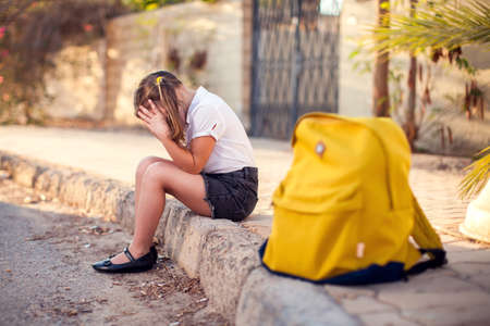 Unhappy pupil with backpack sitting outdoor. Girl feeling stress. Children and emotions conceptの写真素材