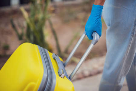 Travel and coronavirus concept. Woman with medical gloves holding luggage on the streetの写真素材