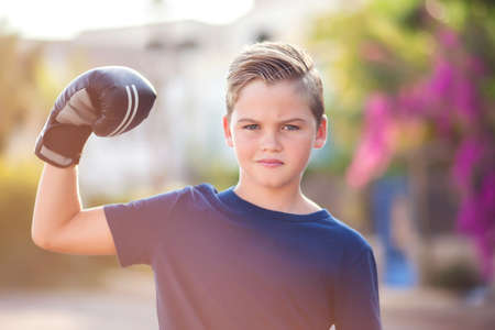 Kid boy with boxing gloves showing strong outdoor. Childhood, leisure and and health conceptの写真素材