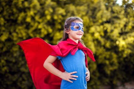 Superhero kid girl against green background outdoor. Childhood, success and and power concept