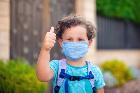 Kid boy with medical face mask showing thumb up gesture outdoor. Coronavirus protection.の写真素材