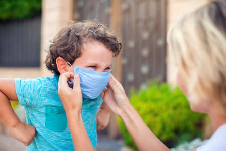 Parent with kid in face mask outdoor. Mother helping angry child to wear facemask during coronavirus and flu outbreak. Virus and illness protectionの写真素材