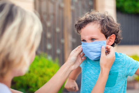 Parent with kid in face mask outdoor. Mother helping angry child to wear facemask during coronavirus and flu outbreak. Virus and illness protectionの写真素材