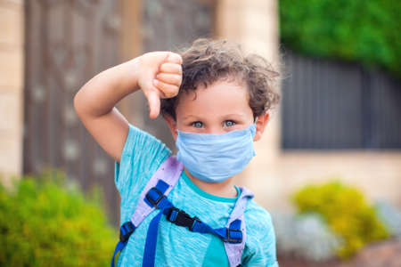 Kid boy with medical face mask showing thumb down gesture outdoor. Coronavirus protection.の写真素材