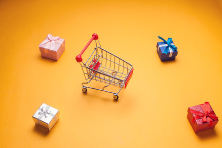 Trolley and gift boxes on yellow background. Shopping and celebration conceptの写真素材
