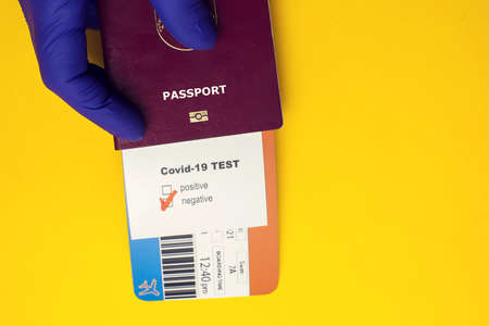 Coronavirus and safety travel concept. Hand holding passport with Covid-19 test with "Negative" mark and airline ticket on yellow backgroundの写真素材