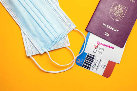 Traveling during COVID-19 pandemic, passport with airline ticket, covid-19 vaccinated card with "Yes" mark, medical mask on yellow background, airport security health and safety check conceptの写真素材
