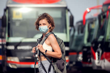 Traveler at the bus station outdoor. Woman with backpack and medical mask waiting for a bus. Travel and tourism conceptの写真素材