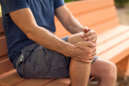 Man with knee pain sitting on the bench in the park. Healthcare and medicine conceptの写真素材