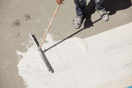 Pool renovation work. A worker applies a layer of waterproofing to the bottom of the pool.の写真素材