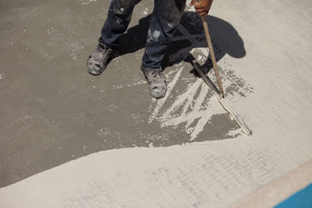 Construction worker laying concrete floor with trowel and putty knifeの写真素材