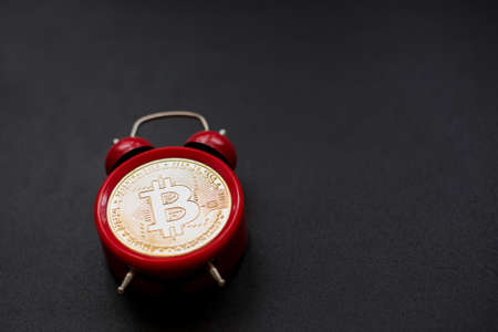 A red alarm clock with a bitcoin coin on a black background.の写真素材
