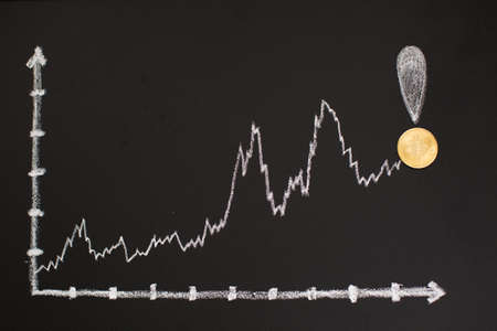 Coins on a blackboard with a chalk drawing of a graphの写真素材