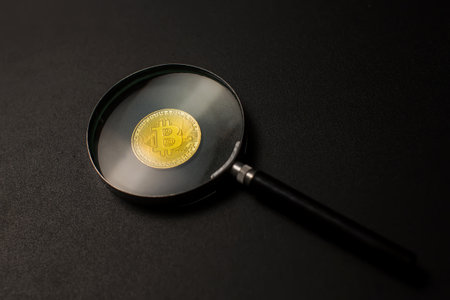 golden bitcoin coin under a magnifying glass on a black background