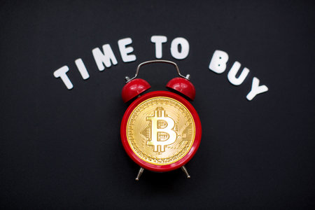 Time to buy bitcoin, alarm clock with bitcoin sign on black background