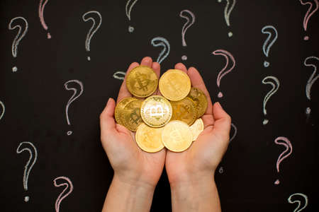A child's hand holds coins against the background of question marks.の写真素材