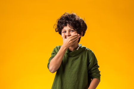 Portrait of laughing kid boy closed mouth with hands.