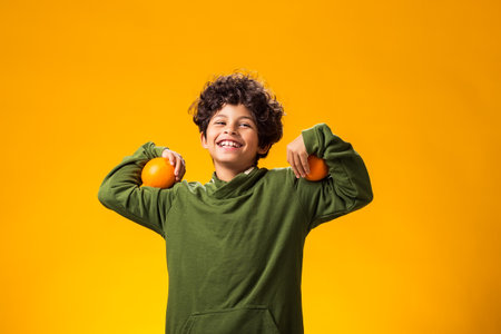 Portrait of child boy holding orange fruits over yellow background. Healthy food conceptの写真素材