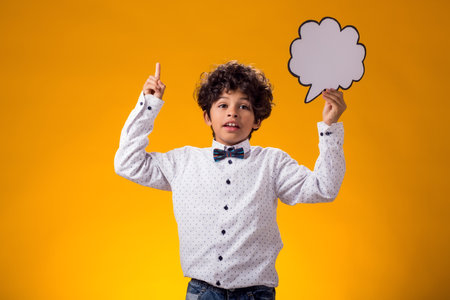 Thoughtful child boy holding speech bubble over yellow background. Education and curiosity conceptの写真素材