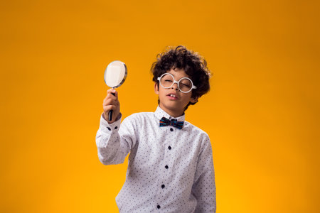 Portrait of child boy looking through magnifier over yellow background. Education and curiosity conceptの写真素材