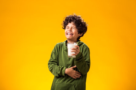 Child boy holding glass of milk over yellow background.の写真素材