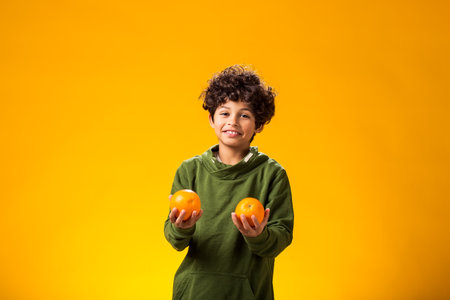 Portrait of child boy holding orange fruits over yellow background. Healthy food conceptの写真素材