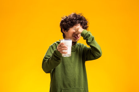Dairy intolerant unhappy child boy holding glass of milk over yellow background.の写真素材