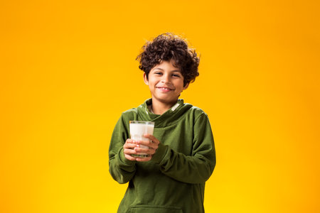 Portrait of smiling child boy holding glass of milk over yellow background. Healthy food conceptの写真素材